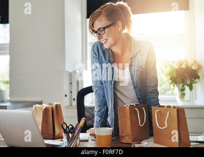 Glücklich Geschäftsfrau arbeiten im home-Office stehen auf ihrem Laptop-Computer, umgeben von Geschenk-Taschen und Verpackungen für t Stockfoto