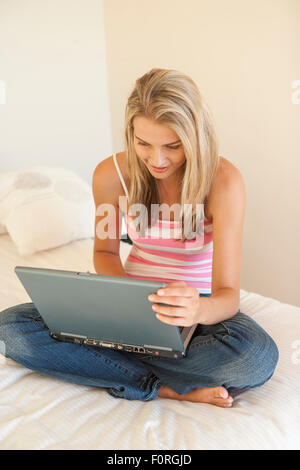 Junge Frau sitzt auf einem Bett in Schriftart eines Laptops Stockfoto