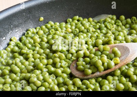 grüne Erbsen in schwarze Pfanne mit Holzlöffel, gedünstetem Gemüse mit Zwiebeln und anderen Kochen Kräutern Stockfoto