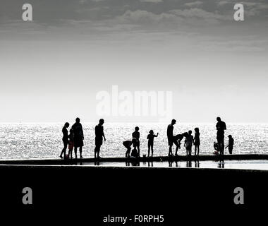 Die Silhouette von Urlaubern stehen am Rand der Gezeiten Planschbecken im Viking Bay, Broadstairs, Kent. Stockfoto