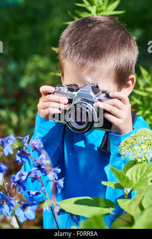 Kleiner Junge mit Retro-SLR-Kamera schießen Makro der blauen Blumen Stockfoto