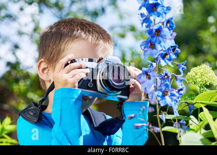 Kleiner Junge mit Retro-SLR-Kamera schießen Makro der blauen Blumen Stockfoto