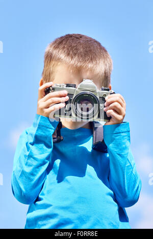 Kleiner Junge mit Retro-SLR-Kamera schießen auf blauen Himmel Stockfoto