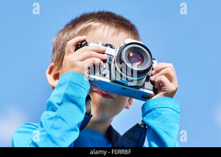 Kleiner Junge mit Retro-SLR-Kamera schießen auf blauen Himmel Stockfoto