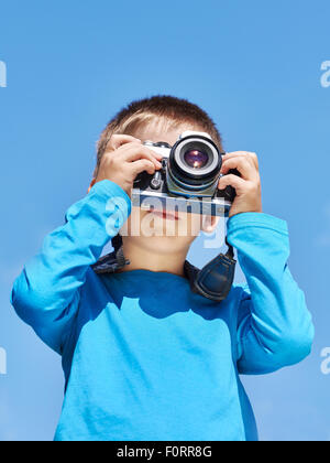 Kleiner Junge mit Retro-SLR-Kamera schießen auf blauen Himmel Stockfoto