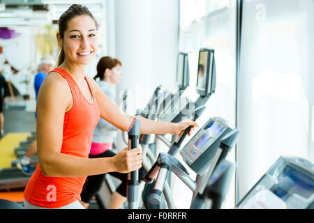 Junge passen Frau mit eine elliptische Trainer in einem Fitnesscenter und lächelnd Stockfoto