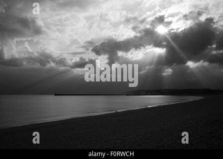 Sonnen-Strahlen durch Wolke über ruhige See und leeren Strand, Seaford, Sussex, schwarz und weiß Stockfoto