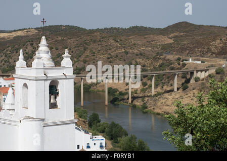 Der Turm der Hauptkirche (Igreja Matriz) von Mértola und der Brücke, die den Fluss Guadiana überquert. Stockfoto