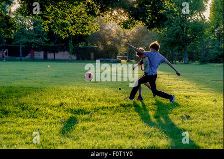 Zwei Jungen spielen Fußball in den letzten der Sommersonne in einem Londoner Park mit ihrem Haustier Hund Stockfoto