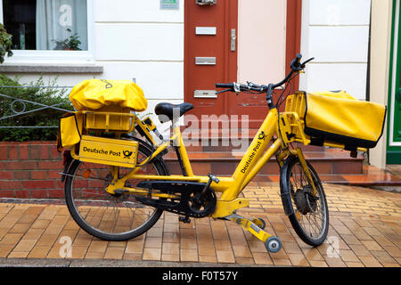 Gelbe Lieferung Fahrrad und Postboten per Deutsche Post DHL weltweit größten Kurier Unternehmen liefert Post im Regen Stockfoto