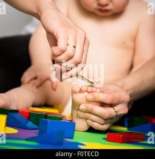 Mutter trimmen Zehennägel auf Füße ihres Babys - Spielzeug herum Stockfoto