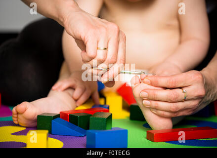 Mutter trimmen Zehennägel auf Füße ihres Babys - Spielzeug herum Stockfoto