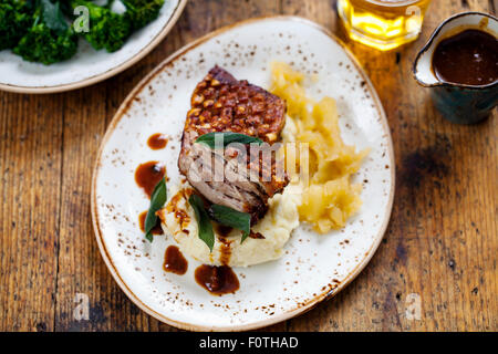 Schweinebauch mit knisternden, Kartoffelpüree, Apfelmus und tief gebratene Salbeiblätter Stockfoto