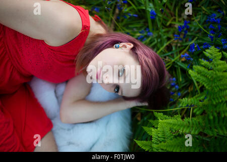 Ein junge Frau Teenager-Mädchen trägt ein rotes Kleid allein in einem Waldgebiet liegend, Frühjahr Abend UK Stockfoto