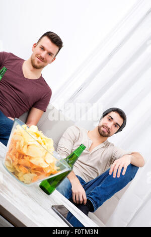 Zwei Jungs vor dem Fernseher, trinken Bier, Chips zu Hause essen Stockfoto