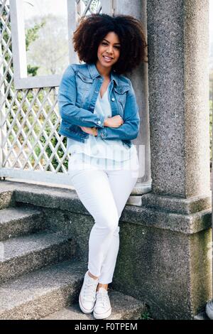 Volle Länge Vorderansicht Mitte erwachsenen Frau, Arme verschränkt, gelehnt Struktur, Lächeln Stockfoto