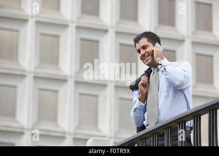 Mitte adult Geschäftsmann mit Jacke über die Schulter mit Smartphone zum Telefon anrufen lassen, Lächeln Stockfoto