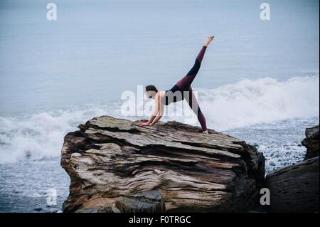 Reife Frau praktizieren Yoga auf Baumstumpf große Treibholz am Strand Stockfoto