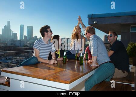 Sechs Erwachsene Freunde trinken Bier am Tisch der Bar auf der Dachterrasse mit Skyline von Los Angeles, USA Stockfoto