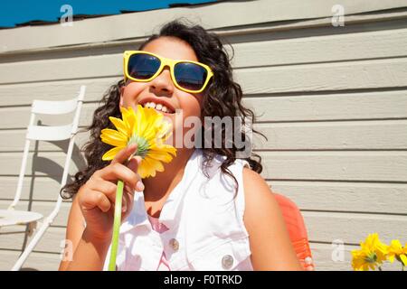 Porträt von Mädchen mit gelben Sonnenbrille hält Sonnenblume auf Terrasse Stockfoto