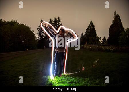 Junger Mann, steht im Feld in der Dämmerung, Arm in Position, Lichtspur tracing Körperform zeigen Stockfoto