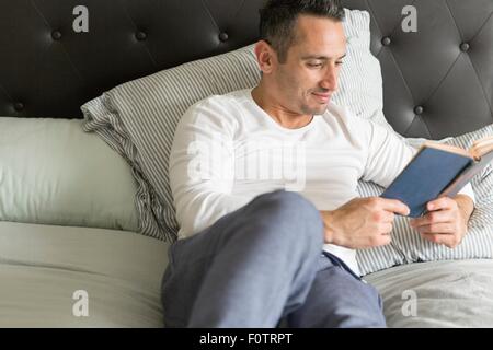Mitte Erwachsener entspannend Mann, auf Bett, Buch lesen Stockfoto