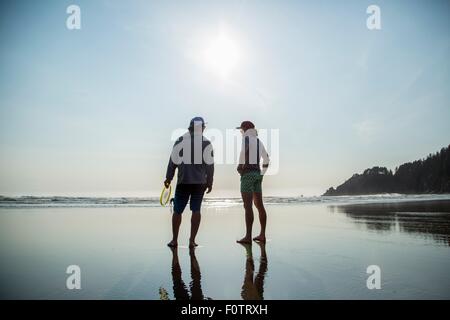 Silhouette Rückansicht von zwei jungen Männern, die im Chat auf Short Sands Beach, Oregon, USA Stockfoto