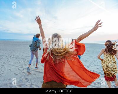 Gruppe von Freunden zu Fuß am Strand, junge Frau mit den Armen in der Luft, Rückansicht Stockfoto