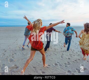 Gruppe von Freunden zu Fuß am Strand, junge Frau mit den Armen in der Luft, Rückansicht Stockfoto