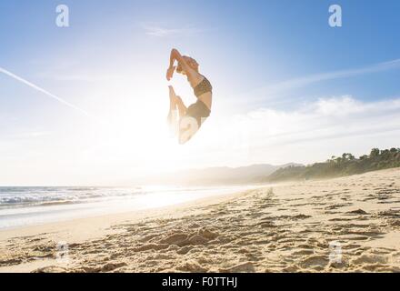 Junge Frau am Strand, springen in die Luft, Sonnenuntergang Stockfoto