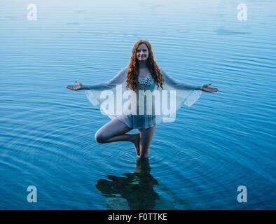 Junge Frau im blauen See, Yoga zu praktizieren Stockfoto