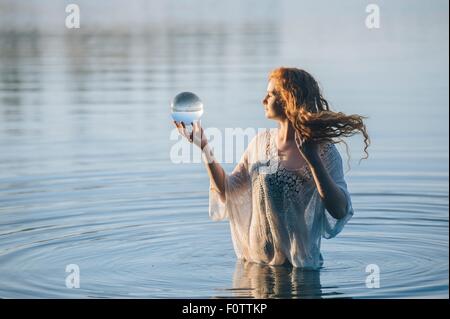 Junge Frau mit langen roten Haaren stehen im See Blick auf Crystal ball Stockfoto