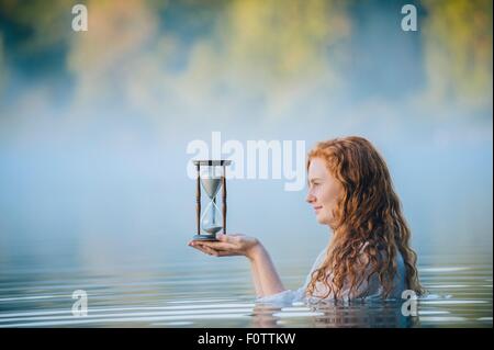 Junge Frau im nebligen See Blick auf Sanduhr Stockfoto