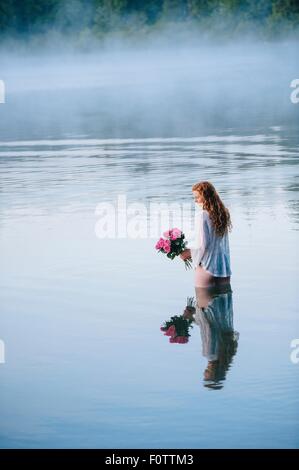 Junge Frau im nebligen See hält Strauß rosa Rosen Stockfoto