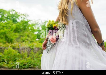 Schuss von junge Frau trägt weißes Kleid tragen Blumenstrauß hinter ihrem Rücken zugeschnitten Stockfoto