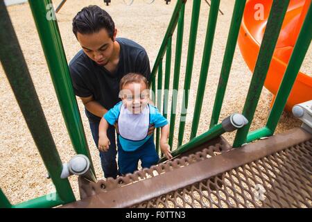 Junger Mann guiding Kleinkind Bruder Spielplatz Rutsche Treppe hinauf Stockfoto