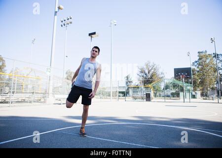 Junge männliche Basketball-Spieler tun Warm up erstreckt sich auf Basketballplatz Stockfoto