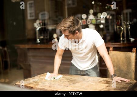 Junger Mann Reinigung Tisch im Wirtshaus Stockfoto