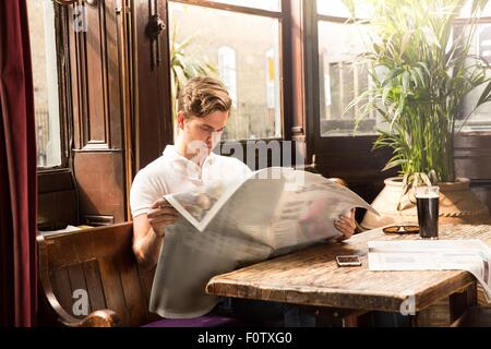 Junger Mann sitzt am Tisch, liest Zeitung Stockfoto