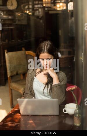 Mitte erwachsenen Frau am Tisch mit Laptop die hand am Kinn Stockfoto