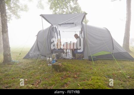 Mutter und Söhne mit Frühstück im Zelt im nebligen Landschaft Stockfoto