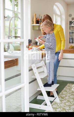 Mutter und Sohn machen, abwaschen, junge auf Stuhl Stockfoto