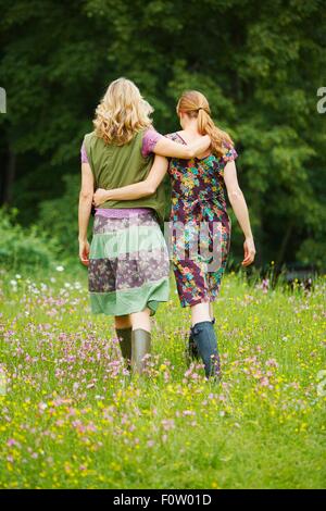 Ansicht von hinten von zwei Frauen, die zu Fuß in Wildblumenwiese Stockfoto