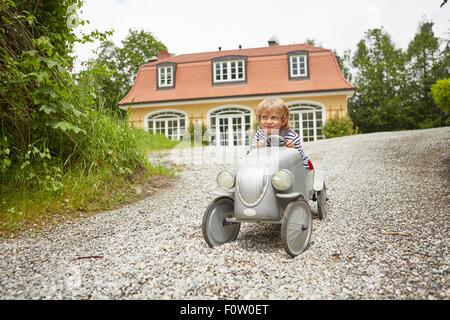 Jungen spielen mit Vintage Spielzeugauto auf Einfahrt vor Haus Stockfoto