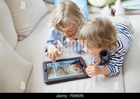 Zwei jungen auf Fronten auf Sofa mit digital-Tablette nebeneinander liegend Stockfoto