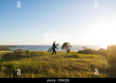 Junge männliche Surfer mit Surfbrett zu Fuß bei Sonnenaufgang Stockfoto