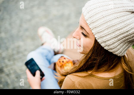 Teenager - Mädchen essen Muffin in der Straße und auf der Suche im Telefon Stockfoto