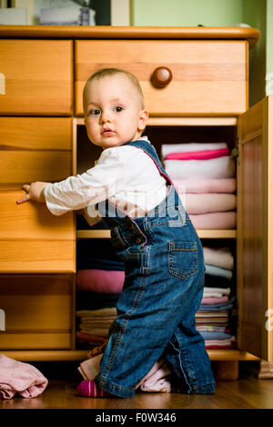 Baby wirft sich Kleider von Holzmöbeln zu Hause Stockfoto