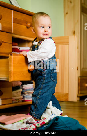 Baby wirft sich Kleider von Holzmöbeln zu Hause Stockfoto