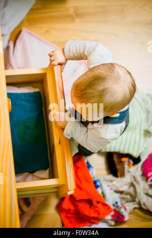 Baby wirft sich Kleider von Holzmöbeln zu Hause Stockfoto